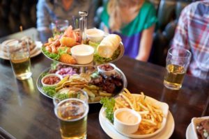 people sitting at table with food and beer at bar